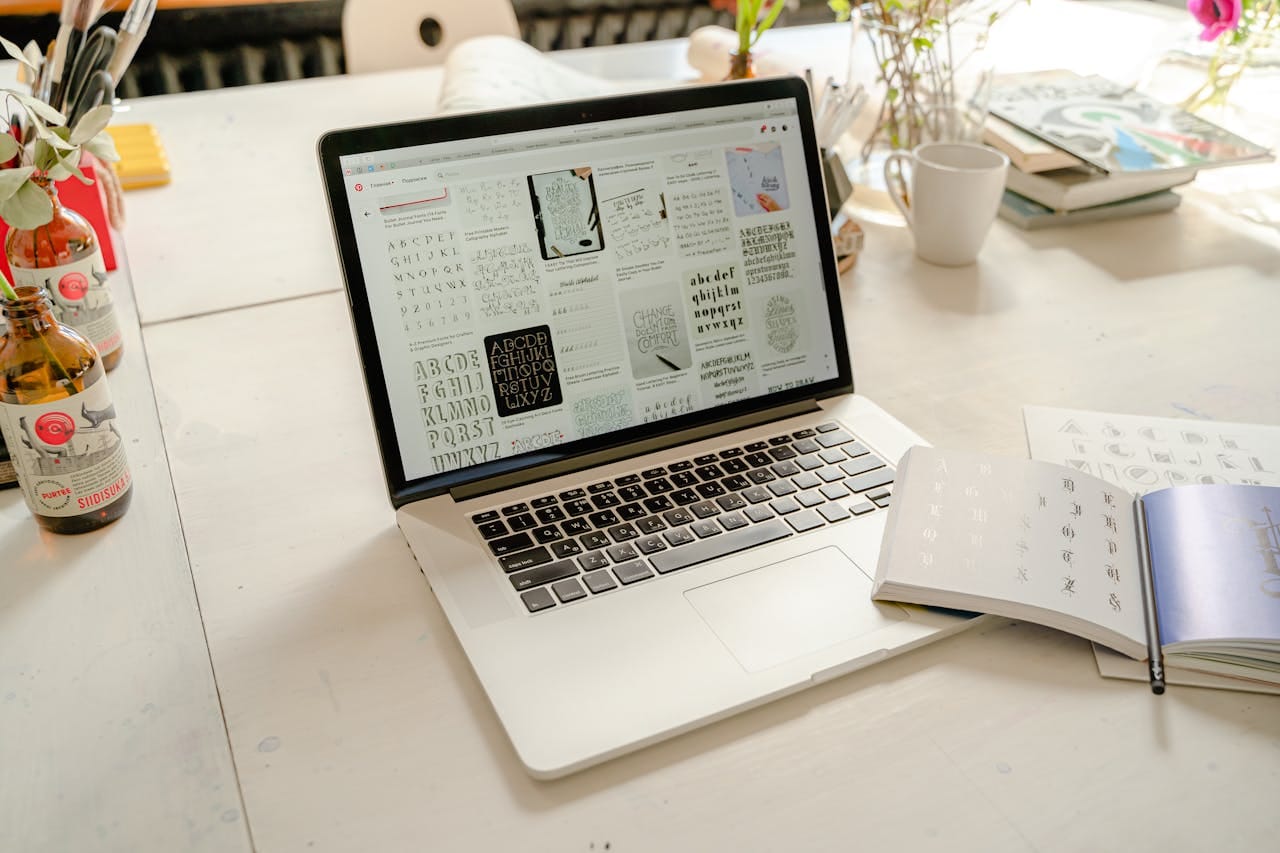 services-02 Bright creative workspace featuring laptop with calligraphy designs, books, and artistic tools.